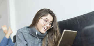 Portrait of smiling young woman lying on couch using earphones and digital tablet